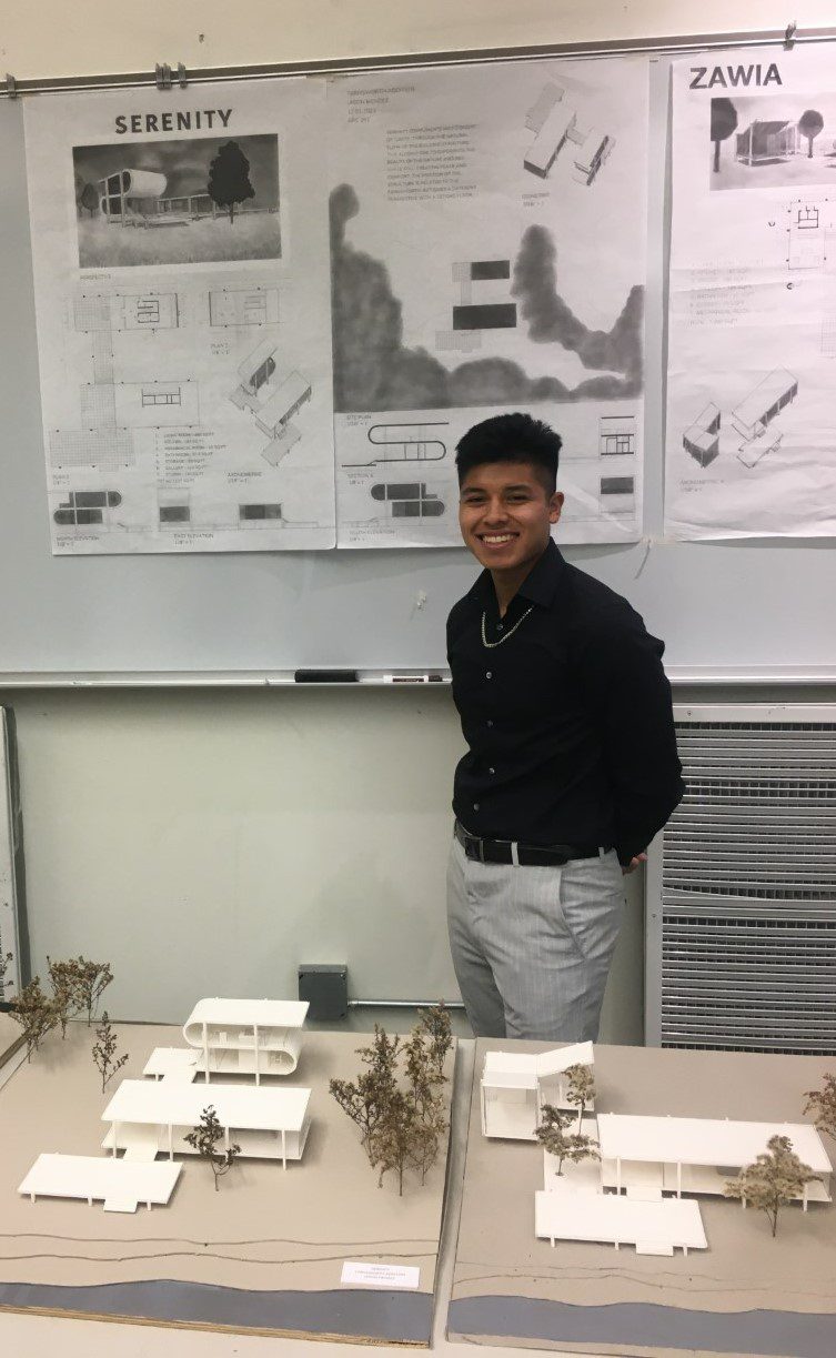 A male ������ student poses in front of a poster with a building design while a 3-D model of the building rests on a table in front of him